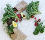 Top view of fresh avocados, kale, tomatoes, and peppers arranged on a marble surface.