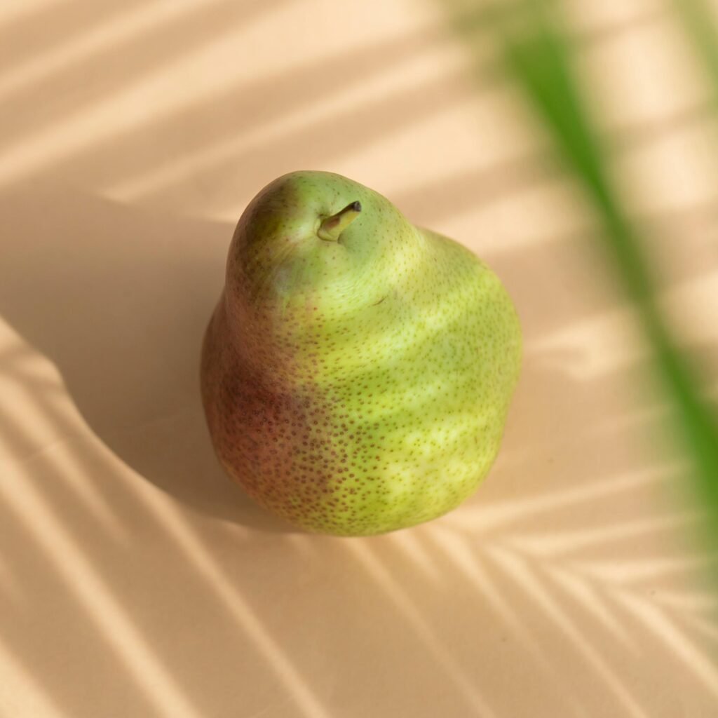 A ripe pear is illuminated by sunlight casting artistic shadows on a warm background.